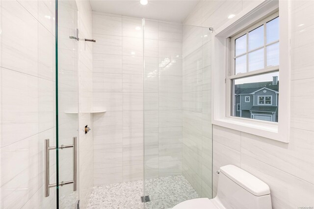 bathroom with a shower with shower door, tile walls, and toilet