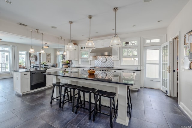 kitchen featuring black dishwasher, decorative light fixtures, white cabinetry, and a center island with sink