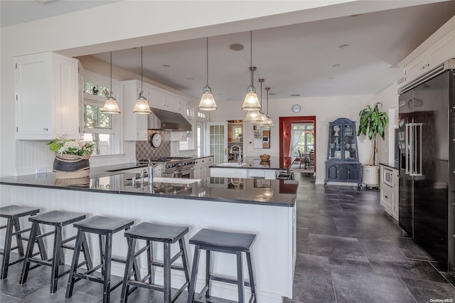 kitchen with kitchen peninsula, black fridge with ice dispenser, a healthy amount of sunlight, decorative light fixtures, and white cabinetry