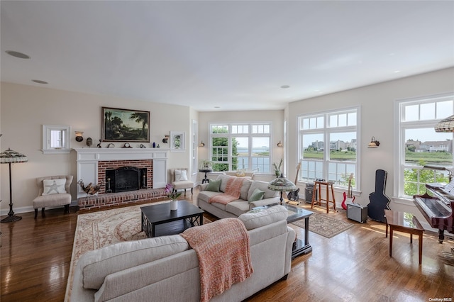 living room with a healthy amount of sunlight, dark hardwood / wood-style flooring, a water view, and a brick fireplace