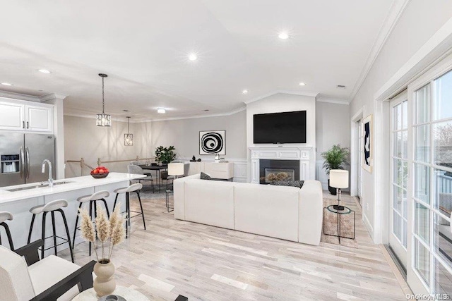 living room with sink, an inviting chandelier, crown molding, light hardwood / wood-style floors, and vaulted ceiling