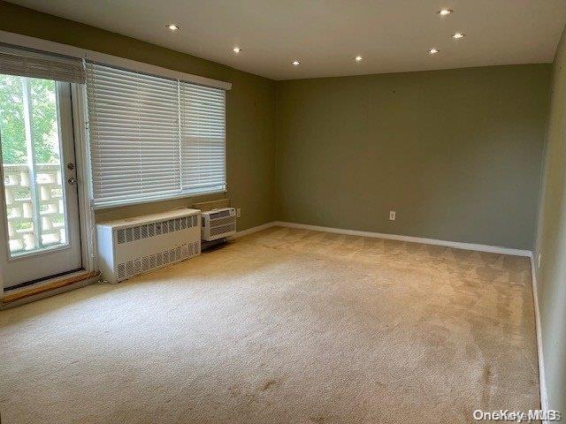 spare room with radiator heating unit, light carpet, and an AC wall unit