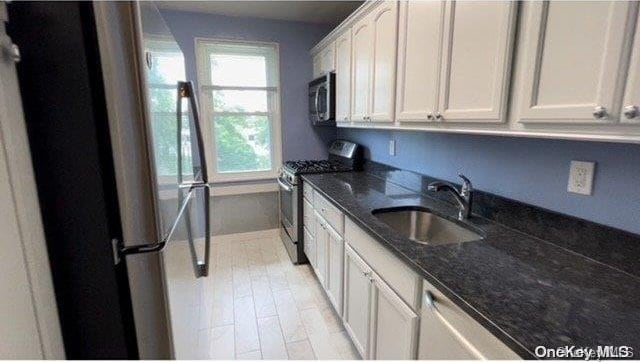 kitchen with white cabinets, sink, dark stone countertops, light wood-type flooring, and appliances with stainless steel finishes