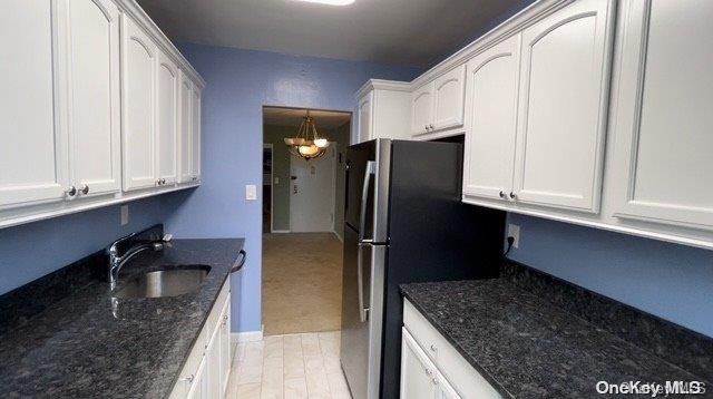 kitchen featuring sink, white cabinets, dark stone counters, and a notable chandelier