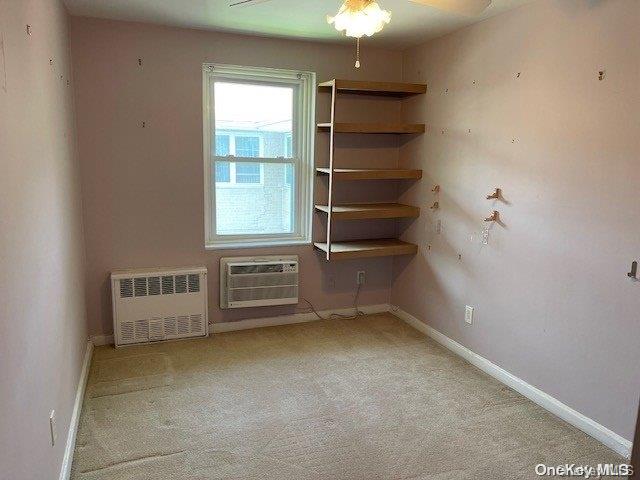 carpeted empty room with radiator, ceiling fan, and a wall mounted AC