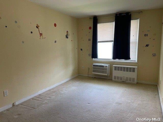 carpeted empty room featuring a wall mounted AC and radiator heating unit