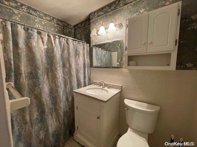 bathroom featuring a shower with shower curtain, vanity, toilet, and tile walls