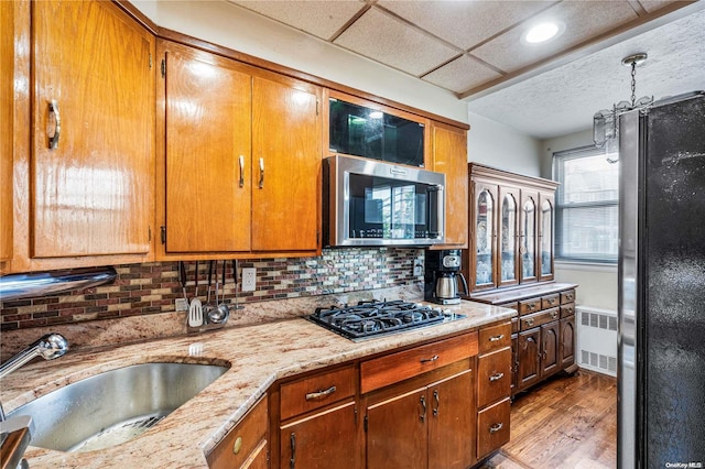 kitchen featuring radiator, sink, backsplash, light hardwood / wood-style floors, and black appliances