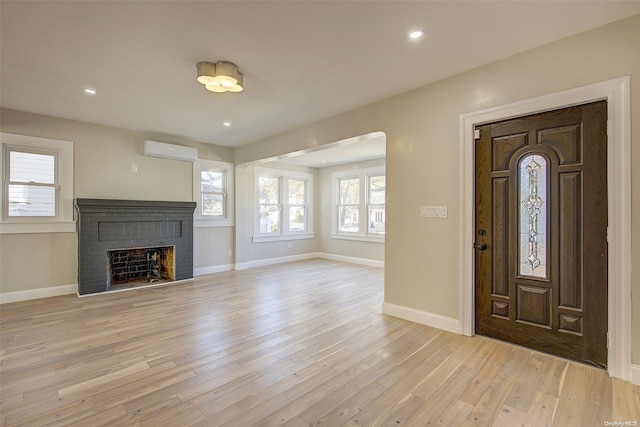 foyer featuring light wood-type flooring, an AC wall unit, and a brick fireplace