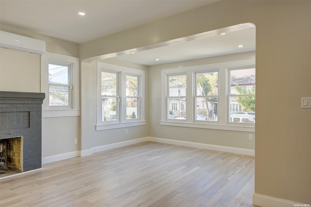 unfurnished living room featuring a wall mounted air conditioner, a healthy amount of sunlight, light hardwood / wood-style floors, and a fireplace