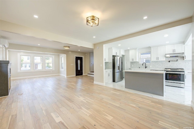 kitchen with white cabinets, appliances with stainless steel finishes, light wood-type flooring, and decorative backsplash