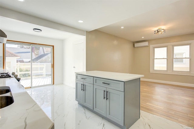 kitchen featuring gray cabinetry, a wall mounted air conditioner, sink, light wood-type flooring, and light stone counters