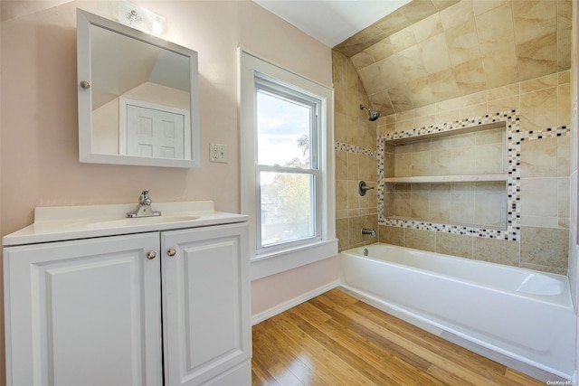 bathroom with wood-type flooring, vanity, vaulted ceiling, and tiled shower / bath