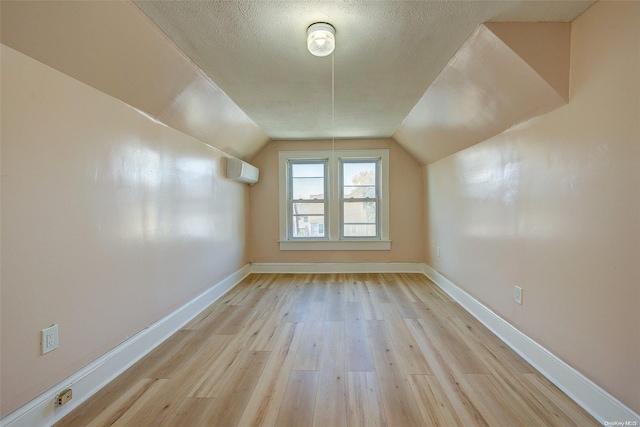 additional living space with light hardwood / wood-style floors, an AC wall unit, a textured ceiling, and vaulted ceiling