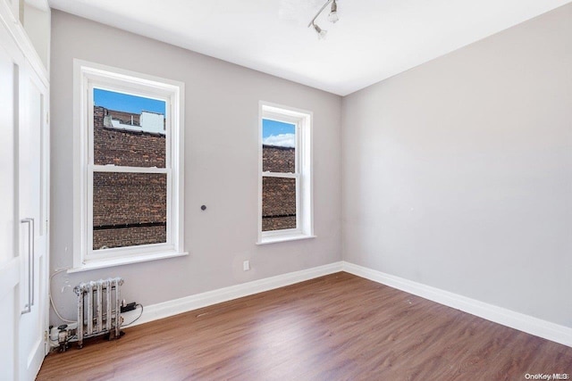 unfurnished room featuring wood-type flooring, radiator heating unit, and track lighting