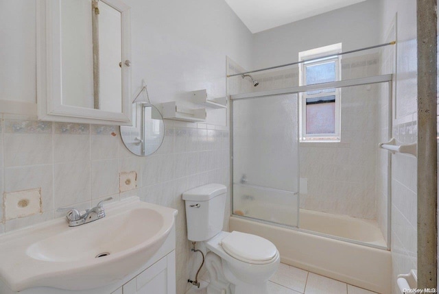 full bathroom with combined bath / shower with glass door, vanity, tile walls, tile patterned flooring, and toilet