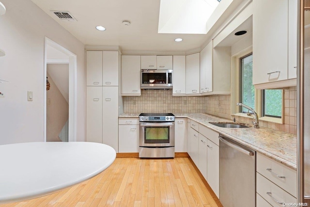 kitchen with sink, white cabinetry, stainless steel appliances, and a skylight