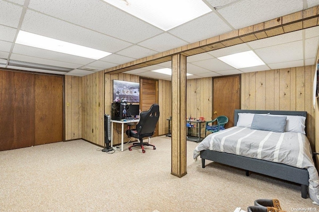 carpeted bedroom featuring a drop ceiling and wooden walls