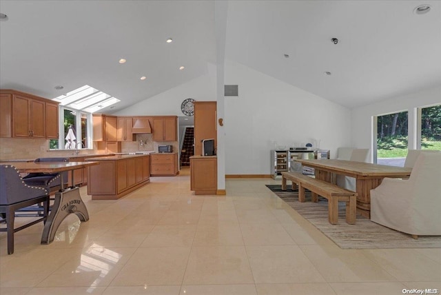 dining space with a skylight, plenty of natural light, light tile patterned flooring, and high vaulted ceiling