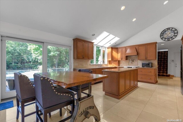 kitchen featuring backsplash, a kitchen island, lofted ceiling with skylight, and light tile patterned flooring