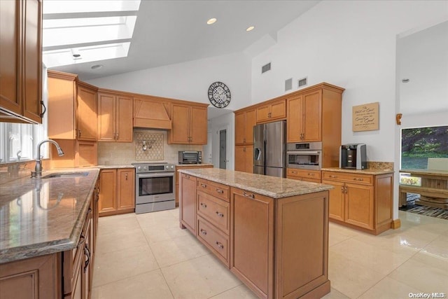 kitchen with a skylight, sink, a center island, light stone counters, and appliances with stainless steel finishes