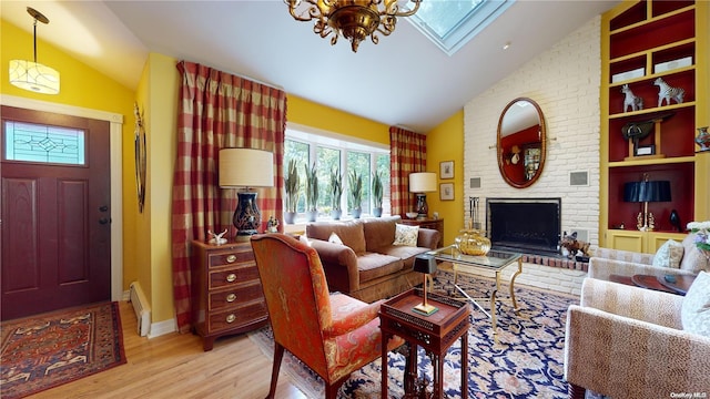 living room with a brick fireplace, a baseboard heating unit, a chandelier, vaulted ceiling with skylight, and light wood-type flooring