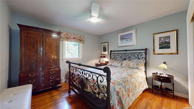 bedroom featuring hardwood / wood-style flooring, baseboard heating, and ceiling fan