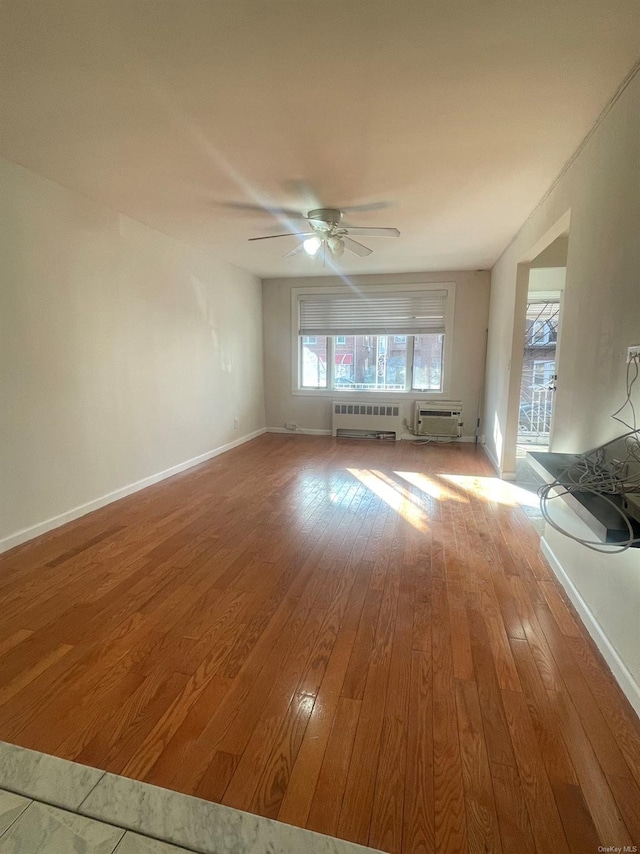 spare room featuring ceiling fan, a wall unit AC, light wood-type flooring, and radiator