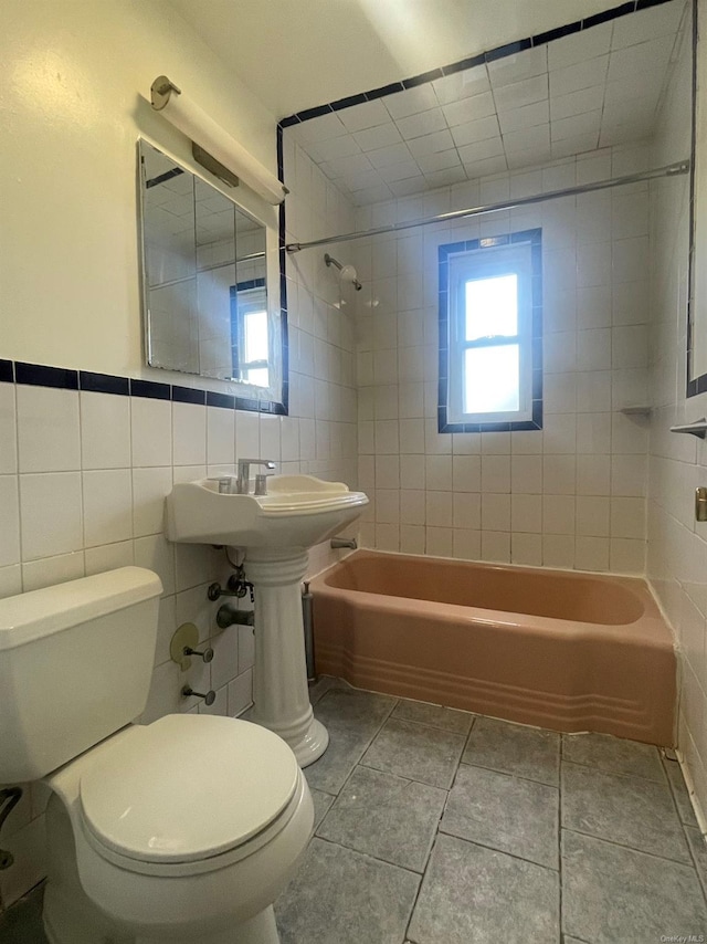 bathroom featuring toilet, tiled shower / bath combo, tile patterned floors, and tile walls