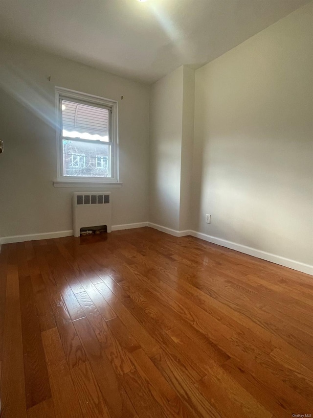 empty room featuring wood-type flooring and radiator heating unit