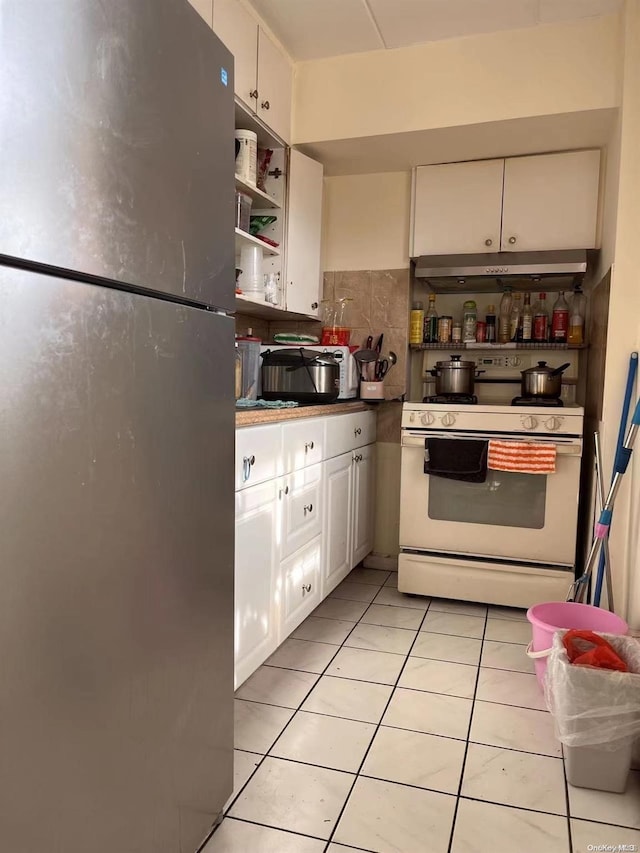 kitchen with white gas range oven, tasteful backsplash, light tile patterned floors, white cabinets, and stainless steel refrigerator