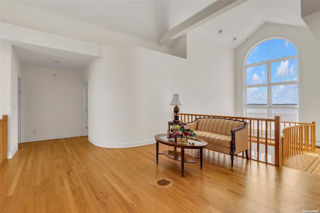 living area with lofted ceiling with beams, a water view, and light wood-type flooring