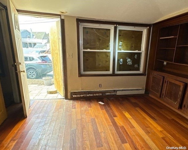 spare room with wood-type flooring, built in features, and baseboard heating