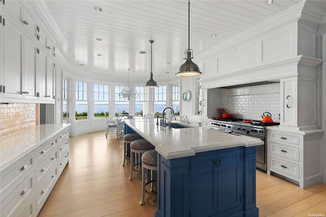 kitchen with stainless steel range, sink, light hardwood / wood-style flooring, decorative light fixtures, and a center island with sink