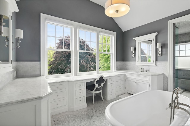 bathroom with tile patterned flooring, a tub to relax in, vaulted ceiling, vanity, and tile walls