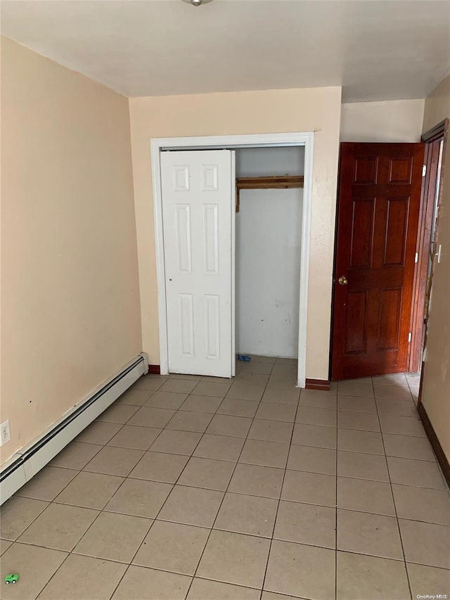 unfurnished bedroom featuring light tile patterned floors, baseboard heating, and a closet