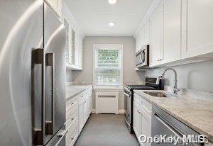 kitchen with white cabinets, stainless steel appliances, light stone countertops, and sink