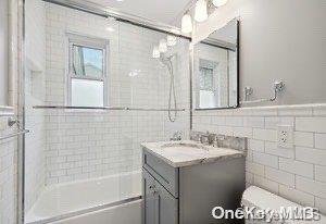 full bathroom featuring vanity, toilet, tile walls, and enclosed tub / shower combo