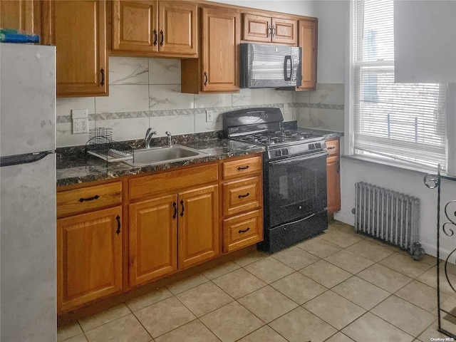 kitchen featuring decorative backsplash, radiator, dark stone counters, sink, and black appliances