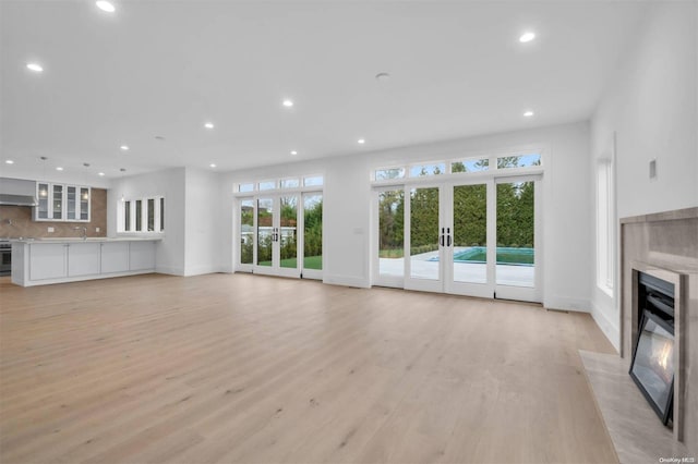 unfurnished living room with light hardwood / wood-style floors, sink, a fireplace, and french doors