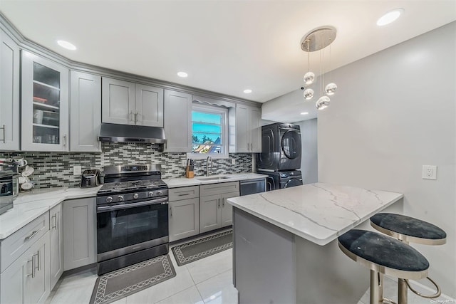 kitchen with stacked washing maching and dryer, stainless steel appliances, sink, pendant lighting, and a breakfast bar area