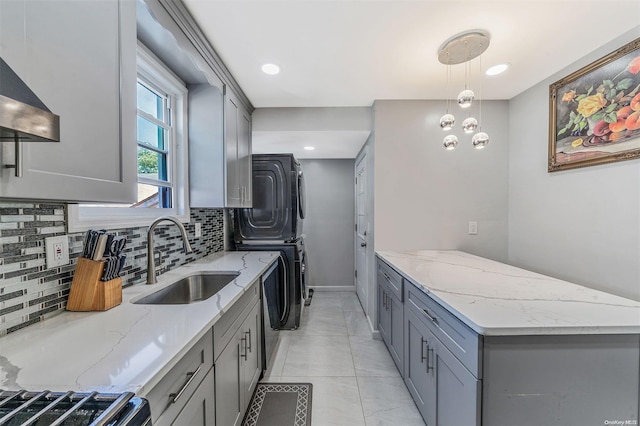 kitchen featuring pendant lighting, stacked washer and dryer, sink, decorative backsplash, and light stone countertops