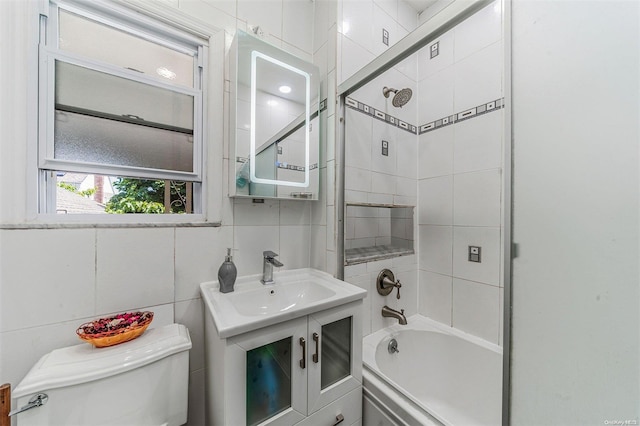 full bathroom with tile walls, vanity, tiled shower / bath combo, and toilet