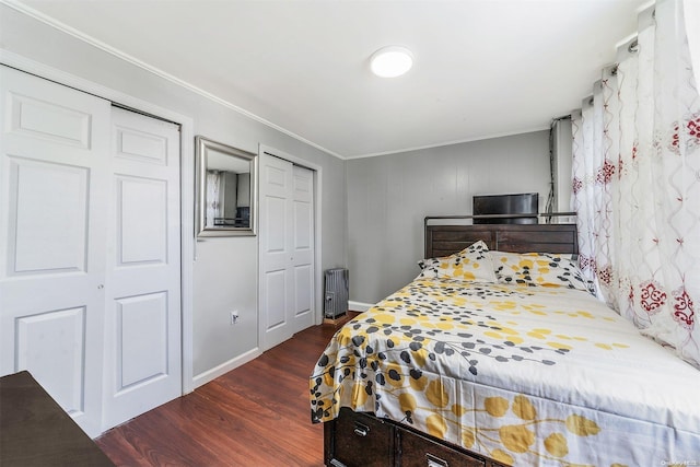 bedroom featuring two closets, dark hardwood / wood-style floors, and ornamental molding