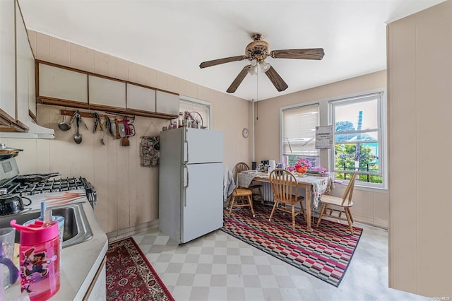 kitchen with ceiling fan, white refrigerator, sink, and wooden walls