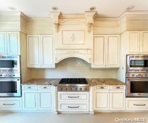 kitchen with cream cabinets, light stone countertops, light tile patterned floors, appliances with stainless steel finishes, and tasteful backsplash