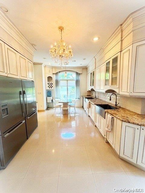 kitchen featuring decorative backsplash, light stone countertops, sink, refrigerator with ice dispenser, and an inviting chandelier