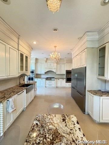 kitchen with black fridge, sink, pendant lighting, stone countertops, and an inviting chandelier