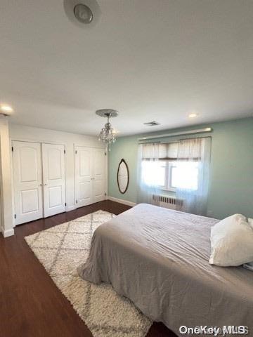 bedroom with radiator heating unit, dark hardwood / wood-style floors, two closets, and ceiling fan