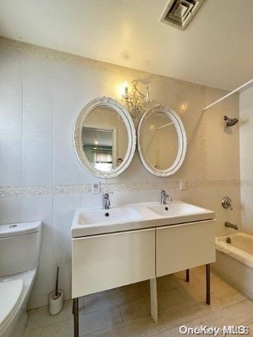 full bathroom featuring tiled shower / bath combo, toilet, sink, and tile walls